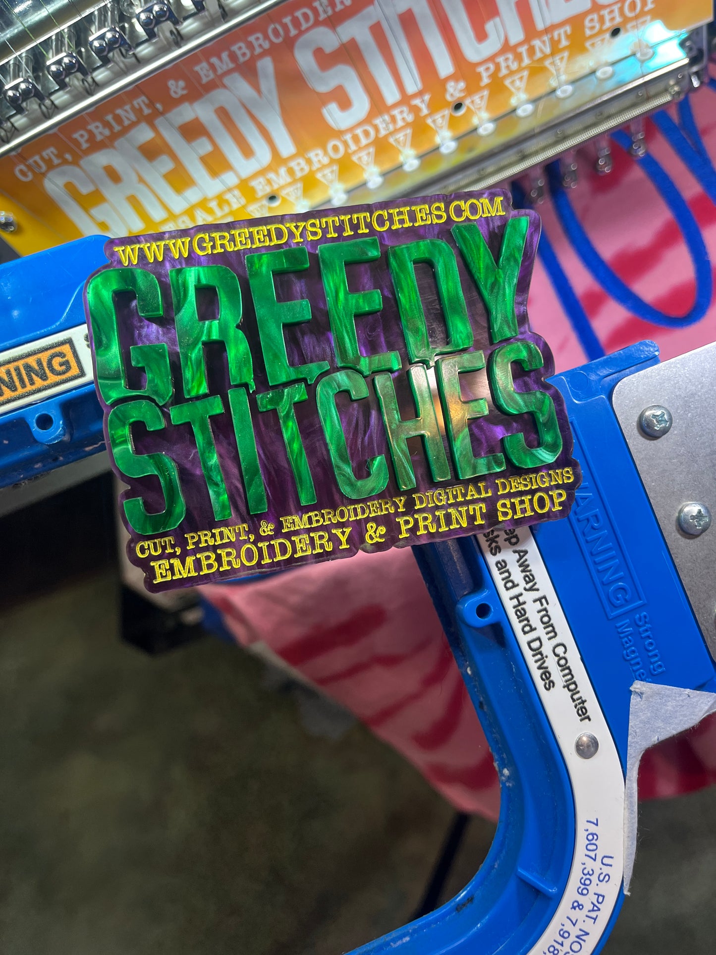 Embroidery machine with a 'Greedy Stitches' label on a blurred background